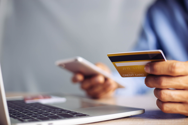 Hand holding a phone and a credit card to pay a bill.